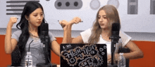 two women are sitting in front of microphones and a laptop that says ' x-in ' on it .
