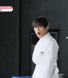 a man in a white lab coat is standing in a dark room and making a funny face .
