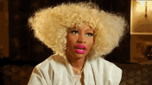 a woman with blonde curly hair and pink lips is wearing a white jacket and necklace