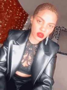 a woman wearing a black jacket and red lipstick looks at the camera
