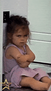 a little girl in a purple dress is sitting on the floor with her arms crossed in front of a sign that says parfum