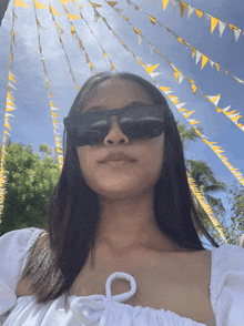a woman wearing sunglasses and a white top stands in front of a row of yellow and white flags