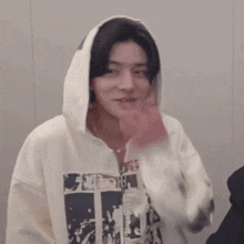 a man is wearing a white hoodie and covering his mouth with his hand .