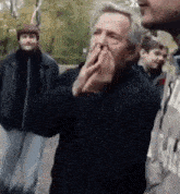 a man with gray hair is covering his mouth with his hands while standing in a crowd .