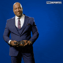 a man in a suit and tie holds a baseball glove in front of a blue background that says fox deportes on it