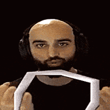 a bald man with a beard is wearing headphones and holding a white object in front of his mouth