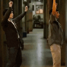 a man and a woman are dancing in a hallway with their arms in the air .