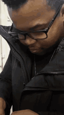 a man wearing glasses and a black jacket is looking down at something
