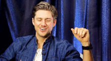 a man in a denim shirt is smiling with his eyes closed and his hand in the air