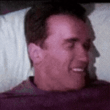 a man is smiling while laying in a bed with his eyes closed .