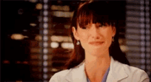 a woman in a lab coat is smiling in front of a window with blinds .