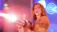 a woman is holding a gun with a red light coming out of it in front of a neon sign .