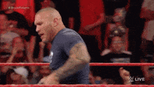 a man in a blue shirt is standing in a wrestling ring with a crowd watching .