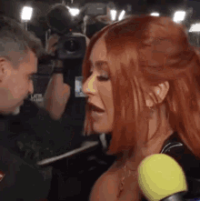 a woman with red hair is talking into a microphone while a man takes a picture .