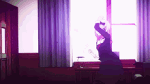 a girl in a black dress is dancing in front of a window in a room .