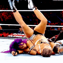 two women are wrestling in a ring with the word royal rumble on the wall behind them