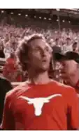a man wearing a red t-shirt with a longhorn on it is standing in front of a crowd of people .