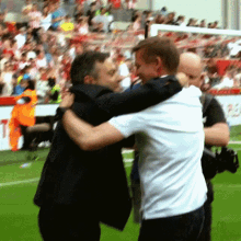a man in a suit and white shirt is hugging another man in a black suit
