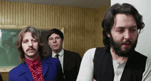 a man with a beard is standing next to two other men in suits