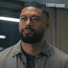 a man with a beard is looking at the camera with a countdown logo behind him