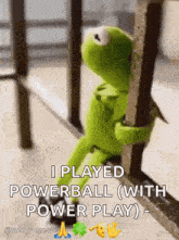 kermit the frog is sitting on a railing holding onto a railing .