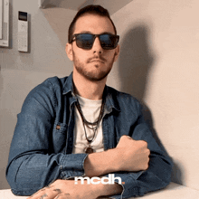 a man wearing sunglasses and a denim shirt has the word mcdh on the bottom