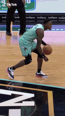 a basketball player in a green jersey is dribbling the ball on the court .