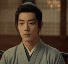 a man in a kimono with a bun on his head is sitting in a chair .