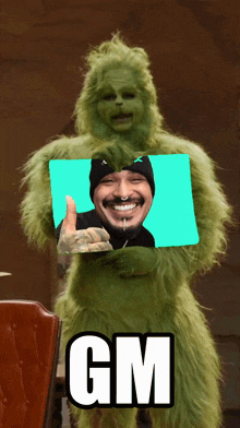 a grinch holding a picture of a man with the word gm below it