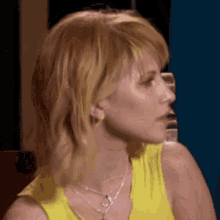 a woman in a yellow tank top and necklace is looking to the side .