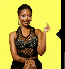 a woman wearing a black top with spikes on it is sitting on a yellow background