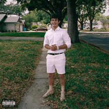 a man in a white shirt and white shorts stands on a sidewalk with a parental advisory sticker on the bottom