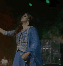 a woman in a blue dress is singing into a microphone while standing on a stage .