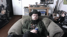 a man in a cowboy hat sits in a chair with a can of soda