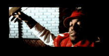a man wearing a red hat and a red jacket is standing in front of a brick wall
