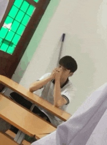 a young man is sitting at a desk in a classroom .