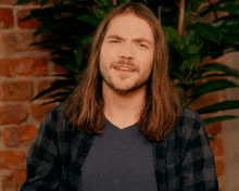 a man with long hair and a beard is smiling in front of a brick wall