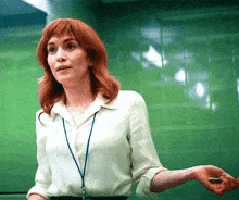 a woman with red hair and a lanyard around her neck stands in front of a green wall