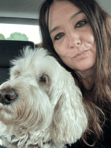 a woman sitting in a car with a white dog