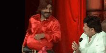 two men are sitting next to each other in front of a red curtain .