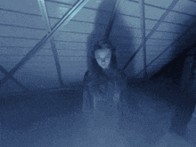 a woman standing in a dark room with a blue light behind her