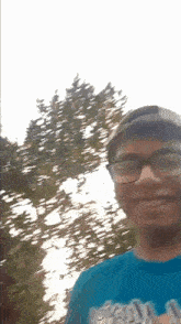 a man wearing glasses and a hat is smiling for the camera while standing in front of a tree