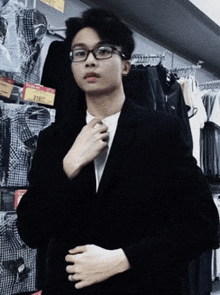a young man wearing glasses and a black jacket is adjusting his tie