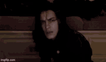 a man with long black hair is sitting on a couch .