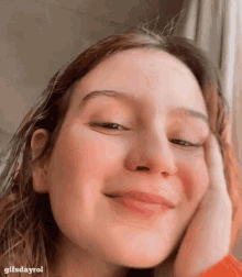 a close up of a woman 's face with her hand on her face and smiling .