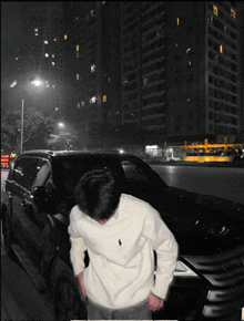 a man in a white polo sweater is standing in front of a black car