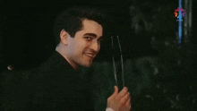 a young man in a black shirt is smiling and holding a piece of glass .