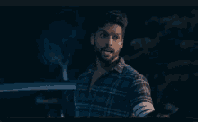 a man in a plaid shirt is holding a cell phone in his right hand