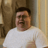 a man wearing glasses and a white shirt is crying in front of a statue
