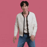 a man wearing a white cardigan and blue jeans is dancing on a pink background